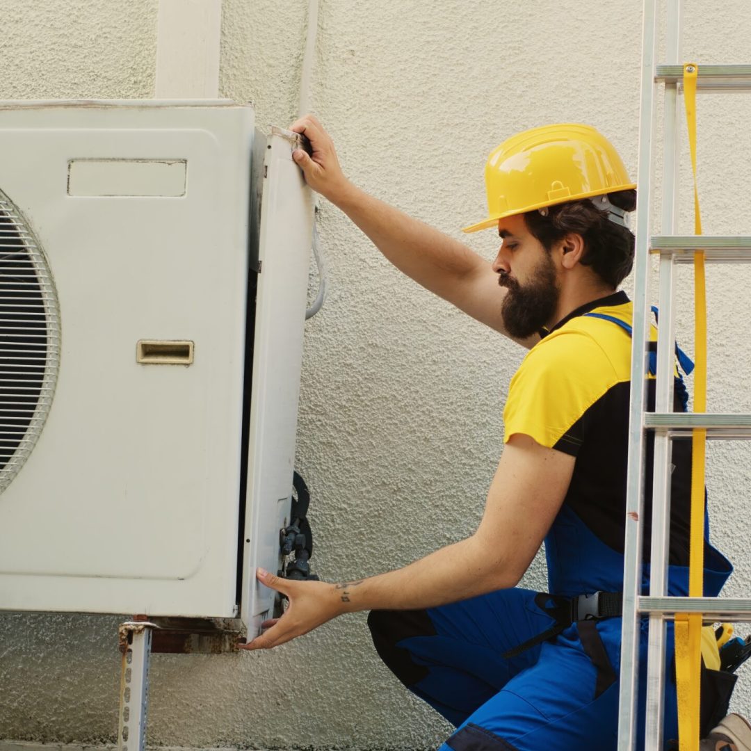 Experienced wireman dissasembling external air conditioner metal side coil panel to check for bad wiring. Meticulous electrician doing repairing on malfunctioning hvac system